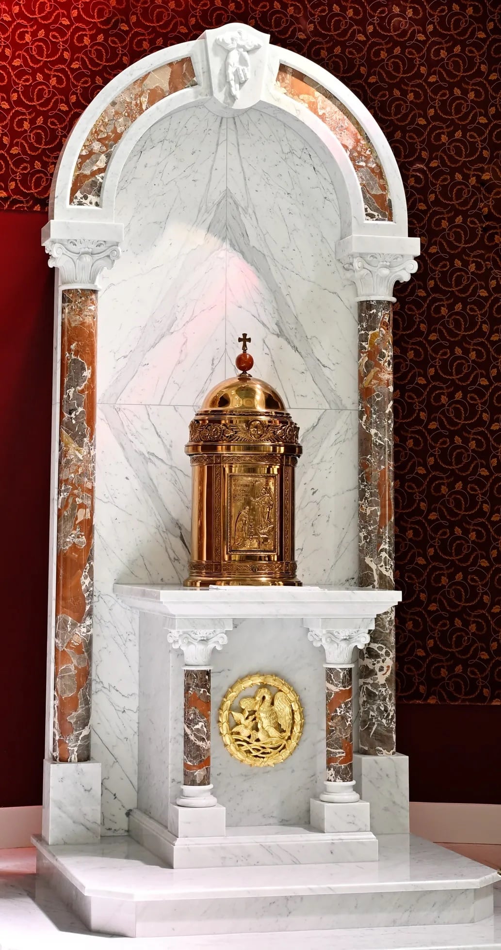 A gold tabernacle on a marble altar, under a marble arch